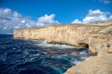Yüksek açılı kireçtaşı kayalıkları ve mavi Akdeniz 'in dalgaları engebeli kıyı şeridi boyunca beyaz bulutlar altında parlak mavi bir gökyüzünün altında..