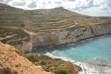 Malta 'da bulutlu bir gökyüzünün altında turkuaz Akdeniz' e kadar uzanan kayalık kireçtaşı kayalıkları ve teraslı yeşil tepelerin yüksek açılı görüntüsü.