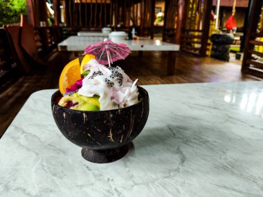 Karışık buzlu tatlı ve meyveli şekerleme bir restoranda hindistan cevizi kasesinde servis ediliyor.