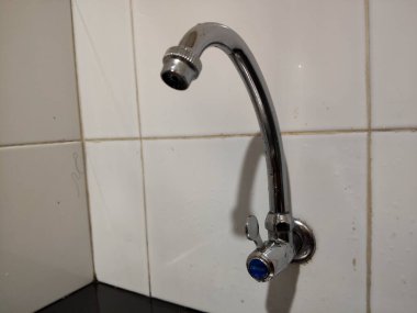 Su musluğu beyaz seramik bir duvara monte edilmiş.