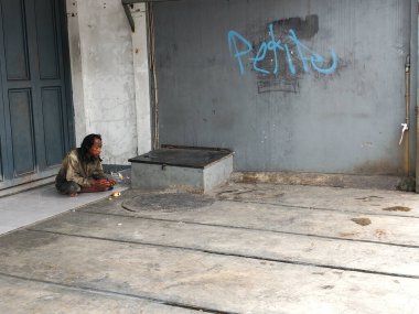 Bandung, Endonezya - 14 Ocak 2026: Kapalı bir dükkanın önünde bir deli oturuyor