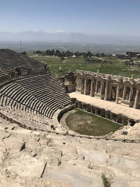 Pamukkale yakınlarındaki Hierapolis harabelerinde antik Roma amfitiyatrosu. Taş koltukları, manzaralı dağ manzarası ve açık mavi gökyüzünün altında arkeolojik alanı olan tarihi bir yer..