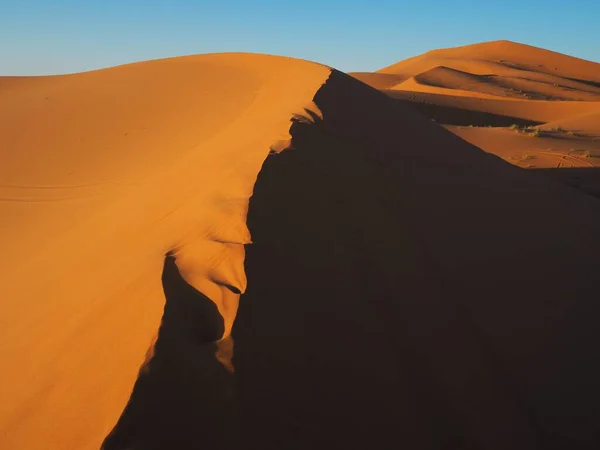 The play of light and shadow among the orange sand dunes of the Merzouga Sahara Desert at sunset. Desert landscape. Travel to Morocco.