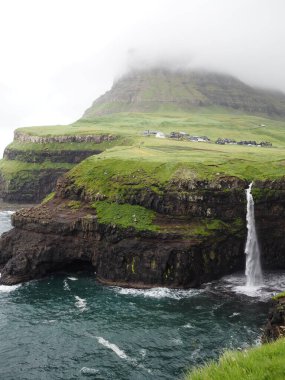 Faroe Adaları 'nın yeşil manzaraları. Atlantik Okyanusu 'na akan Mulafossur şelalesinin inanılmaz manzarası. Gasadalur Köyü, Vagar Adası.