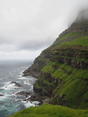 Faroe Adaları 'nın yeşil manzaraları. Dik kıyı kayalıkları ve bulutlu bir günde Atlantik okyanusu, Vagar Adası.