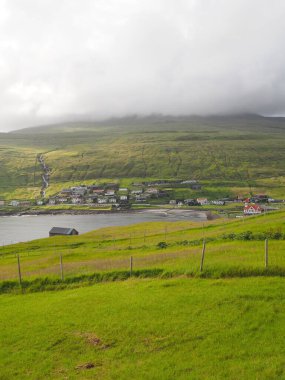 Faroe Adaları 'nın yemyeşil kuzey manzaraları. Sandavagur, Vagar Adası 'ndaki küçük sahil köyü etrafında şelalesi olan yeşil çayırlar ve tepeler..
