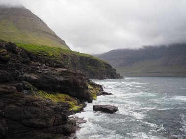 Faroe Adaları 'nın kuzey manzaraları. Sert Kuzey Atlantik Okyanusu, Vidareidi Köyü, Vidoy Adası kıyılarındaki yeşil kayalıkların ve fiyortların dramatik manzarası.