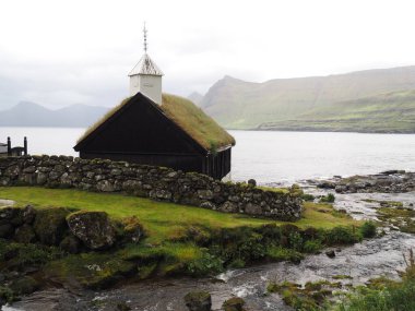 Faroe Adaları 'nın yeşil kuzey manzaraları. Funnings Kirkja - yeşil fiyortların arasında çimen çatılı geleneksel Faroe kilisesi, Funningur köyü, Eysturoy Adası.