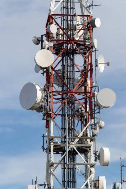 Uydu antenleri ve iletişim ekipmanlarıyla kırmızı ve beyaz telekomünikasyon kulesi. 