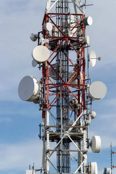 Uydu antenleri ve iletişim ekipmanlarıyla kırmızı ve beyaz telekomünikasyon kulesi. 