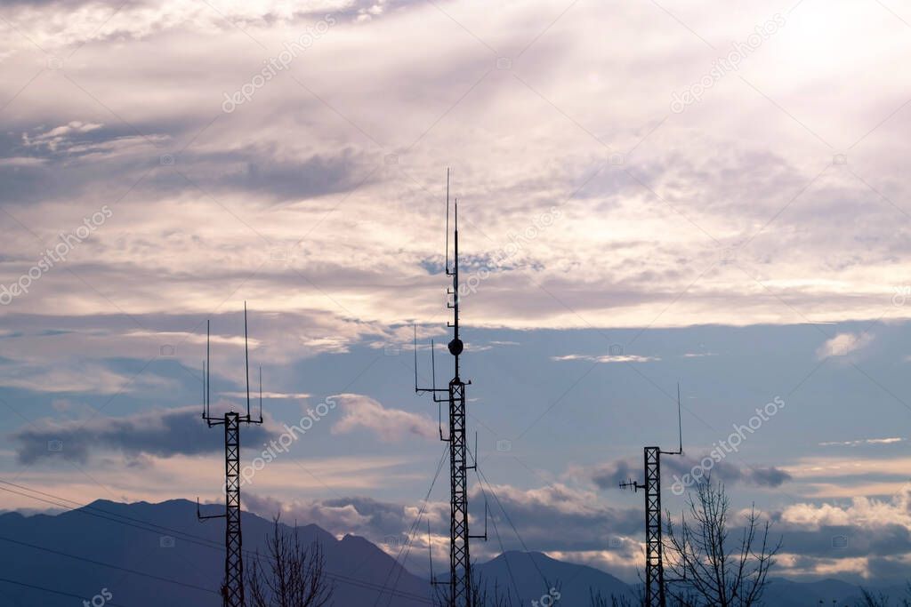 Three telecommunication masts or mobile towers with satellite antennas silhouettes at the sunset cludy sky background.