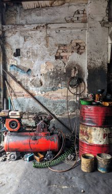 Yağ tankı, kompresör ve atölye araçlarını gösteren bir otomotiv veya tamirhanenin içi.