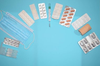 Haplar, tıbbi maske, eldivenler ve mavi arka planda termometre..