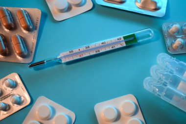 Mavi arka planda haplar ve termometre.