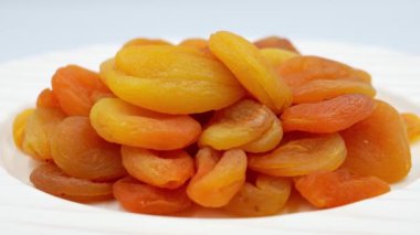 Beyaz arkaplanda, tabakta yavaşça kurumuş kayısıları döndürüyor.