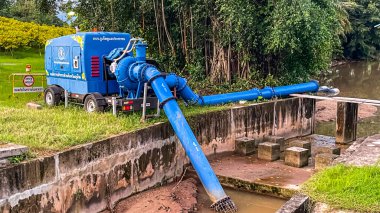 Tayland, Phuket - 1 Kasım 2025: Mavi bir mobil pompa bir boru hattına bağlanıyor ve çamurlu bir kanaldan su pompalıyor..