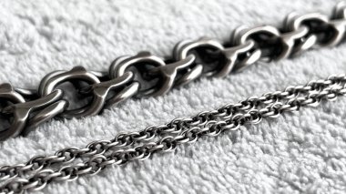 Açık renkli tekstil yüzeyinde çeşitli dokuması olan gümüş mücevherlerin yakın çekimi. Mücevherlerin kavramsallaştırılması, metalin değeri, minimalizm ve yüksek kalite..