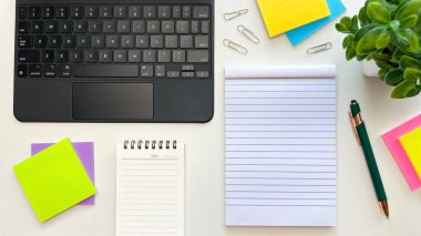 Boş sayfaları, dizüstü bilgisayarı, renkli yapışkan notları, ataçları ve beyaz bir masa üzerinde bir kalem olan bir defter. Planlama, üretkenlik ve ofis işleri için kavramsal fikirler.