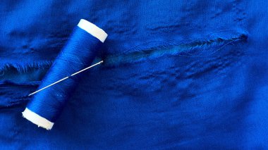 Mavi kumaştaki yırtığın yakın plan çekimi. Bir makara iplik ve iğneyle. Konsept olarak giysi tamiri, tekstil restorasyonu ve el dikimi ile ilgili..