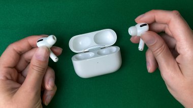 Kablosuz kulaklığı olan bir adam yeşil arka planda açık bir şarj davasının yanında. Kavramsal olarak, modern teknolojiyi tasvir eder, müzik dinlemek, mobil cihazlar, ve her gün kullanılan aletler..