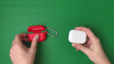 Bir kadının elleri silikon koruyucu kılıfı yeşil arka planda kablosuz kulaklığa yerleştirir. Kavramsal olarak, bu cihazların, elektronik aksesuarların ve modern teknolojinin korunması anlamına gelir..