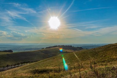 a beautiful landscape of the hills and a field under the bright sunlight on sunset