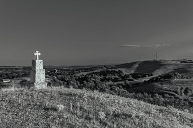 a vertical shot of a beautiful white cross on a hill in black and white