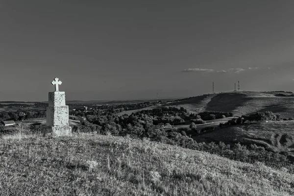 a vertical shot of a beautiful white cross on a hill in black and white