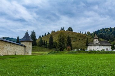 Ağaçlarla çevrili yeşil çimlerin dikey görüntüsü ve arka planda bulutlu bir gökyüzünün altında bir kilise.