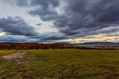 Renkli sonbahar yapraklarıyla tarlanın üzerinde dramatik bulutlar.