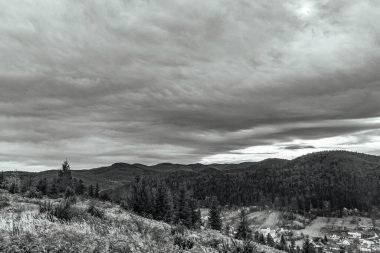 Ormanın üzerindeki siyah beyaz bulutlar ve dağlardaki ağaçlar.