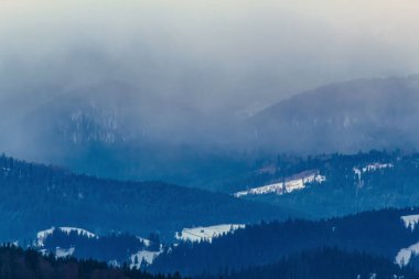 Kış manzarası, karla kaplı dağlar, sisli ağaçlar.