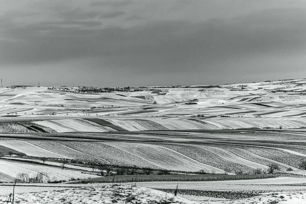 Kış tarlaları ve karlı tepeleri olan bir manzara..