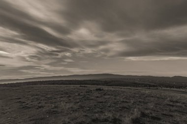 Gökyüzünde bulutlar olan bir dağ manzarasının dikey gri tonlu görüntüsü.