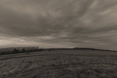 Bulutlu gökyüzünün bir tarlanın üzerindeki gri tonlu görüntüsü.