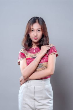 Sakin ve düşünceli bir ifadeyle kendinden emin bir Asyalı kadın, kollarını ileri bakarken nazikçe kavuşturuyor, gücünü, zarafetini ve modern kadınsı duruşunu profesyonel bir pozda temsil ediyor..