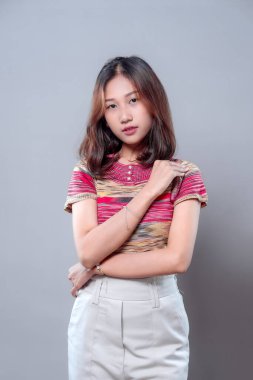 Kendine güvenen Asyalı bir kadın, sakin ve zarif bir pozla, renkli bir bluz ve açık renk pantolon giyerek, güzellik, profesyonellik ve modern kadın özgüveninin bir karışımını sergiliyor..