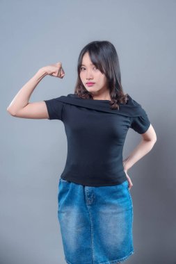 Güçlü bir duruş sergileyen kendine güvenen Asyalı bir kadın kolu esnemiş, güç, kararlılık ve motivasyonunu ifade ediyor. Onun cesur ifadesi kendine güveni ve iç gücünü yansıtıyor..