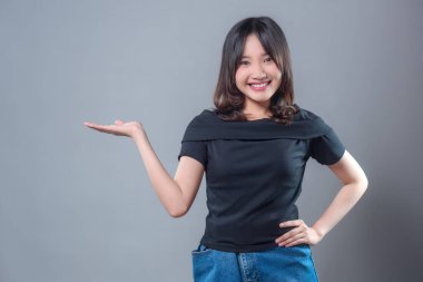 Siyah bluz ve kot etek giyen neşeli bir Asyalı kadın tek eliyle gösterirken özgüvenle gülümsüyor. Reklam ve promosyon için uygun bir jest yapıyor ve sunuyor..