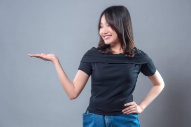 Siyah bluz ve kot etek giyen gülümseyen Asyalı bir kadın, elleri yanda, kendinden emin ve dostane bir ifade sergiliyor, sunum veya reklam kavramları için mükemmel..