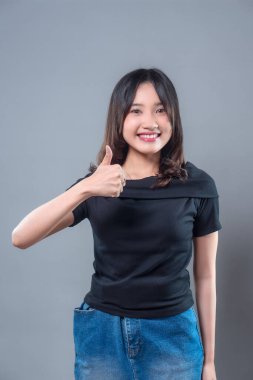 Siyah gömlek ve kot etek giyen gülümseyen Asyalı bir kadın olumlu bir jest yapıyor, olumlu, güven ve onay gösteriyor, başarıyı, teşvikleri ve iyimser tutumu temsil ediyor..