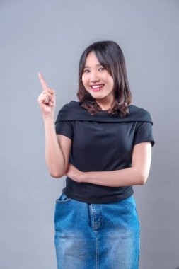 Neşeli Asyalı bir kadın, tek parmakla yukarıya doğru gülümserken, pozitif bir fikir ve güveni ifade ederek, yaratıcılığı ve iyimserliği temsil ediyor..