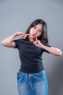 Şakacı bir Asyalı kadın, yanaklarını şişirip parmaklarını göstererek, neşeli, esprili ve pozitif kişiliğini gündelik bir şekilde göstererek sevimli bir yüz ifadesi takınıyor..