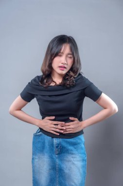 Acı dolu bir ifadeyle karnını tutan Asyalı bir kadın rahatsızlığını ve karın ağrısını gösteriyor. Görüntü mide ağrısı, kramp ya da sindirim sorunları gibi sağlık sorunlarını gösteriyor..