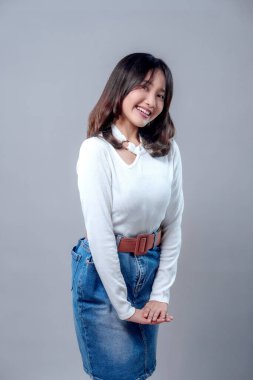 Beyaz bir kazak ve kot etek giyen, samimi ve doğal bir pozla gülümseyen neşeli, genç bir Asyalı kadın. Neşeli ifadesi güven, zarafet ve pozitifliği yansıtıyor..