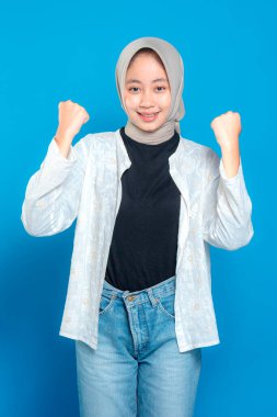 Tesettürlü genç bir kadın, iki eli de havada, özgüvenle gülümsüyor, başarıyı, kararlılığı ve coşkuyu ifade ediyor. Yüzündeki ifade motivasyon ve güçlü bir ruh veriyor..