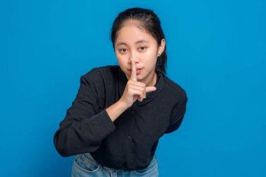 Ciddi ifadeleri olan genç bir kadın sessiz bir jest yapmak için parmaklarını dudaklarına koyuyor, sessizliği ya da gizliliği simgeliyor, gizlilik ve gizlilik hakkında reklam kavramları için ideal..