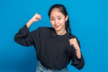 Genç bir Asyalı kadının portresi sıkıca tutulmuş bir yumruğu kaldırırken özgüvenle gülümsüyor. Onun cesaret verici yüz ifadesi motivasyon, kararlılık ve reklam kullanımı için pozitif enerji taşır.