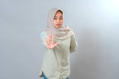 Ciddi, tesettürlü genç Müslüman bir kadın kameraya bakarken elini kaldırıyor. Onun katı yüz ifadesi kendine güveni ve net sınırlar gösteriyor..