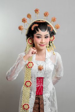 Solo Putri kılığında Endonezyalı gelin altın bir başlık ve yasemin çelenk giyiyor. Nazik bir gülümseme ve yumrukla poz veriyor. Kendine güveni, zarafeti ve kültürel gururu simgeliyor..